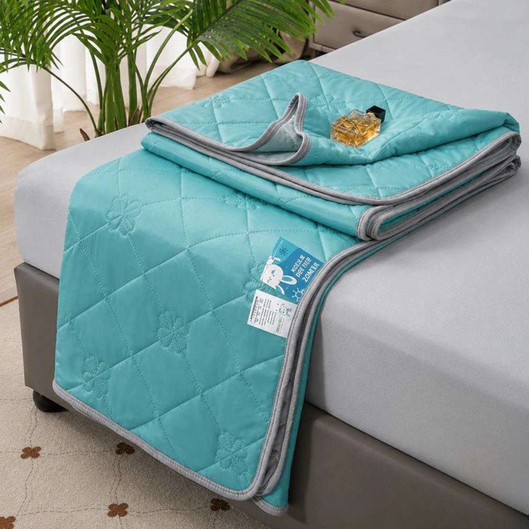 Aquamarine quilted blanket folded on a bed, folded corner showing gray trim and a fabric care tag.