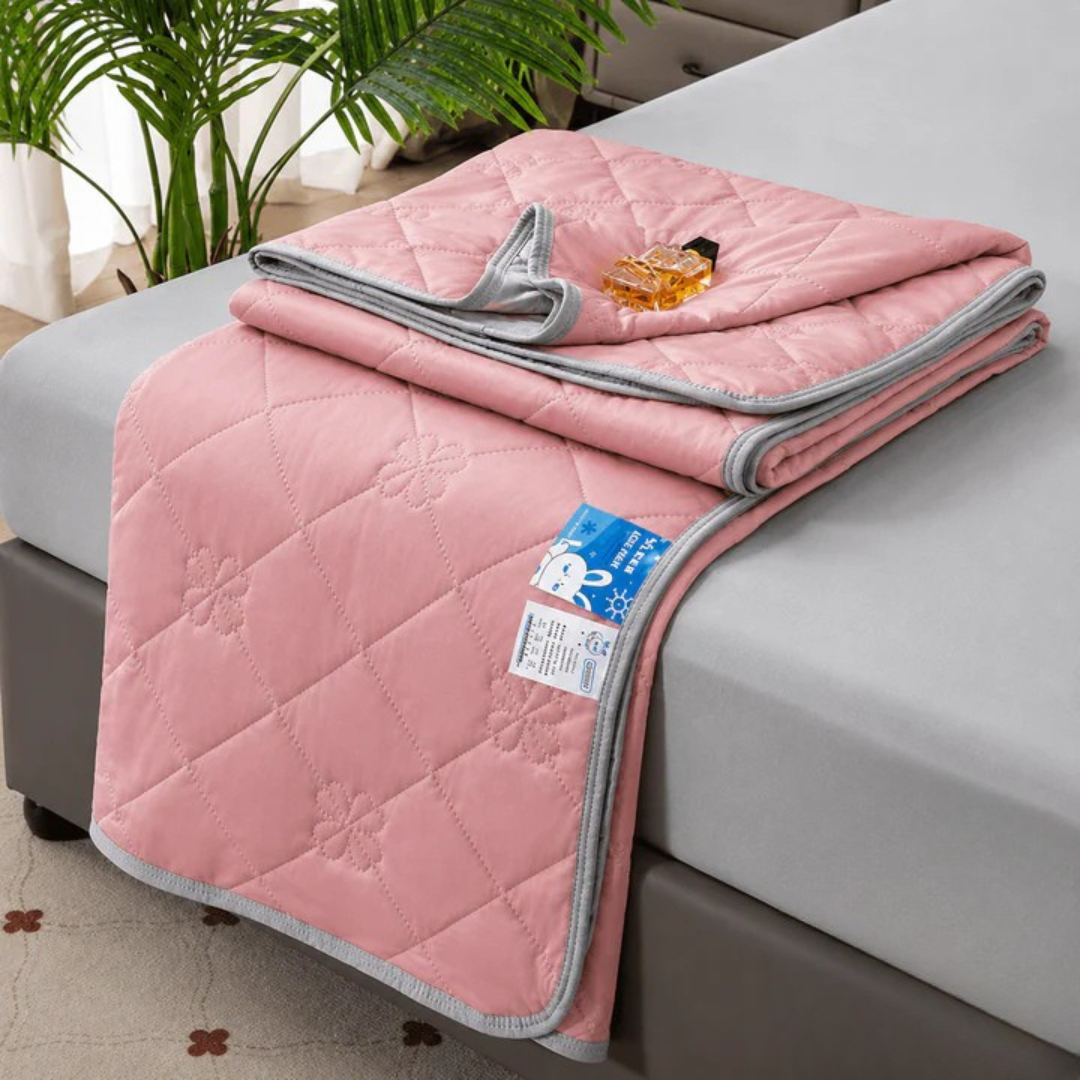 Pink quilted blanket folded on a bed, folded corner showing gray trim and a fabric care tag.