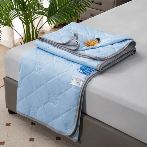 Light blue quilted blanket folded on a bed, folded corner showing gray trim and a fabric care tag.